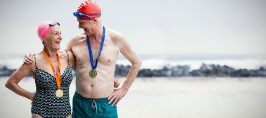 Composite image of senior couple in swimwear wearing medals
