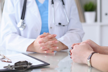 Close up of a doctor and  patient hands discussing something while sitting at the table