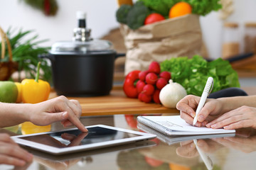 Close-up of  human hands are gesticulate over a tablet in the kitchen. Friends having fun while choosing menu or making online shopping