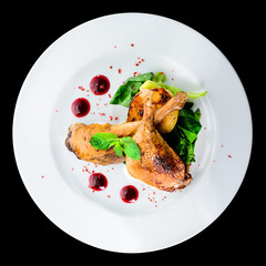 Juicy delicious cooked duck legs served with herbs and sauce in a white plate isolated on black background. Autumn menu in an Italian restaurant. Top view, flat, overhead