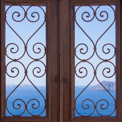 wooden door with carved pattern on the glass. Sea and blue sky on the background, Santorini Greece
