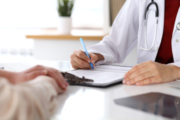 Close up of a female doctor filling up  an application form while consulting patient