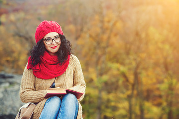 Attractive young woman reads book in a park and enjoys sunny autumn day.