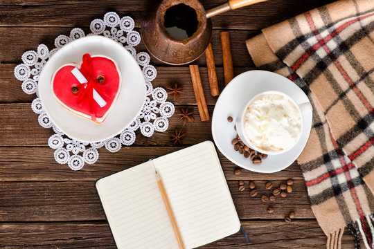 Cozy rest. Cappuccino, heart shaped cake, a notebook with a pencil, pots of coffee. Top view