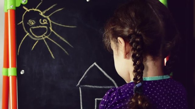A little girl draws a dream house on a malbert with colored crayons.