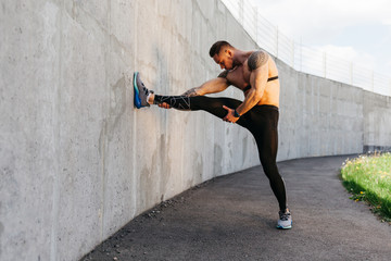 Fototapeta premium Portrait of sportsman stretching legs in gray wall background