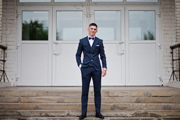 Portrait of a handsome high school graduate in stylish tuxedo posing on the stairs on the prom.