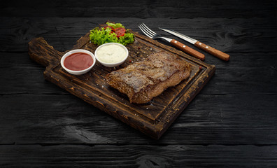 Grilled beef steak with sauces on a board. Dark wooden table.