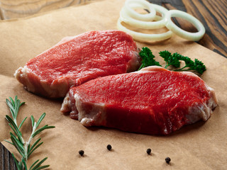 Fresh raw pork steaks on a craft paper on wooden background