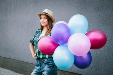 Happy young woman in plaid shirt and hat standing with balloons and smiling