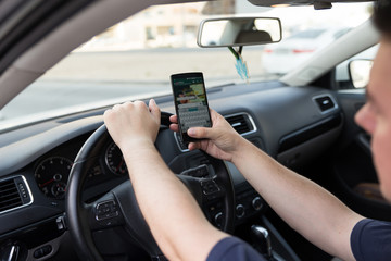 Plakat Man texting while driving. Using a smartphone while driving. Side view of man driving while using mobile phone.