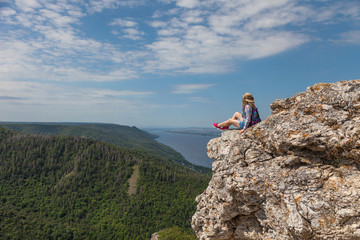 A young woman sits on a mountain and looks at a beautiful view