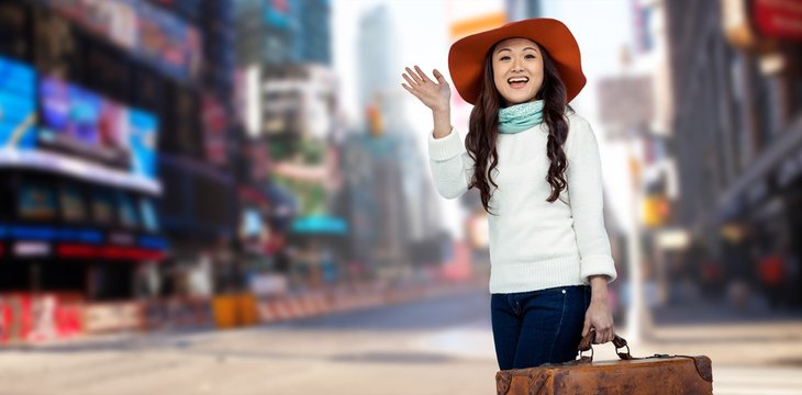 Composite image of asian woman with hat holding luggage 