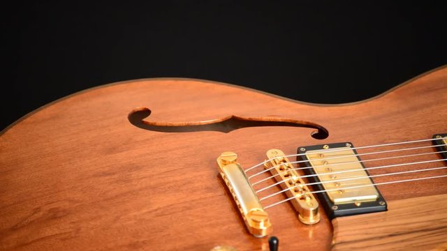 Detail of bridge, strings and efes of a jazz electric guitar gyrating at black background