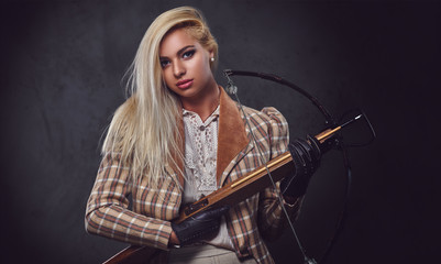 Studio portrait of blond old fashioned female holds a crossbow.