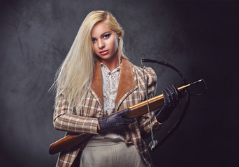Studio portrait of blond old fashioned female holds a crossbow.