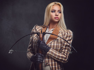 Studio portrait of blond old fashioned female holds a crossbow.
