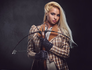 Studio portrait of blond old fashioned female holds a crossbow.