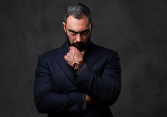 Serious, bearded male dressed in a grey suit.