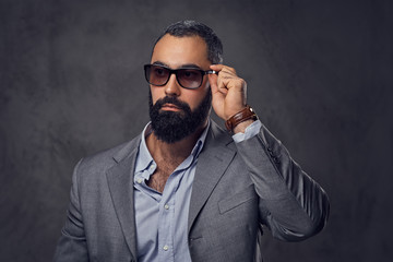 Studio portrait of bearded male dressed in a suit and sunglasses.