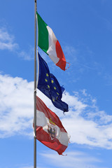 The Italian, Austrian and Eu flag blows in the wind at Lake Garda, Italy.