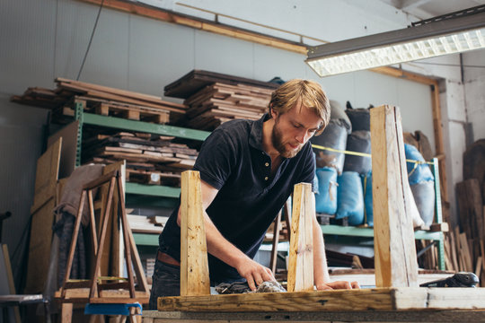 Young man applying oil to wooden table in workshop