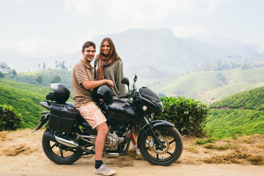Couple smiling on a motorbike on a country road surrounded by tea plantations and mountain scenery