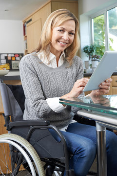 Disabled Woman In Wheelchair Using Digital Tablet At Home