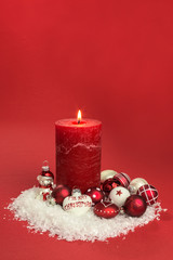 red candle with red and white christmas baubles on snow