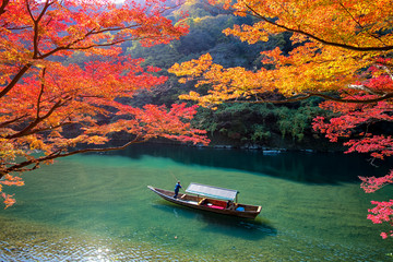 Obraz premium Boatman punting łodzi dla turystów, aby cieszyć się jesienią widok wzdłuż brzegu rzeki Hozu w Arashiyama Kyoto, Japonia.