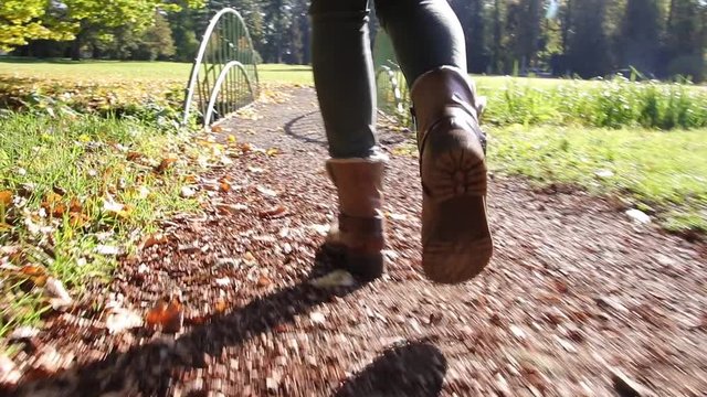 Young tourist woman with leather boots is walking over a bridge in park. Autumnal season. Double slow motion taken from a low angle. 