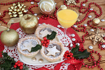 Christmas mince pies tarts with holly on a heart shaped plate with eggnog, gold bauble decorations and red bead strand on oak table background. 