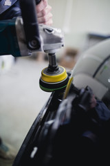 Car detailing - Hands with orbital polisher in auto repair shop. Selective focus.