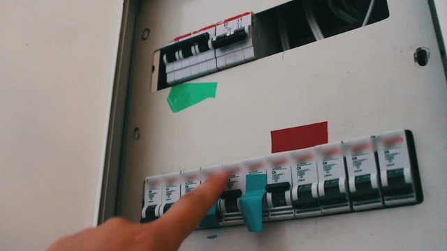 The female hand turns on and off the toggle switch on the electrical panel that hangs on wall