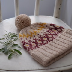 Beige knitted cap of wool with a pompon on a white wooden background