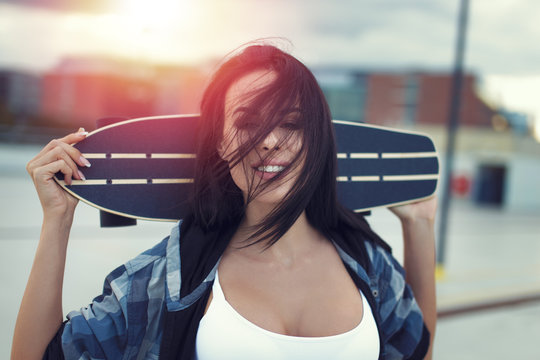 Young woman holding skateboard in sunset portrait