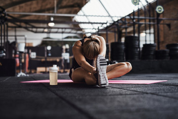 Fototapeta na wymiar Fit young woman doing stretches on a gym floor