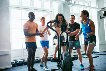 Smiling people supporting their friend riding a stationary bike