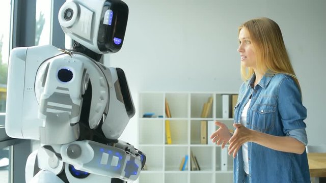 Cheerful girl gesturing while talking with robot