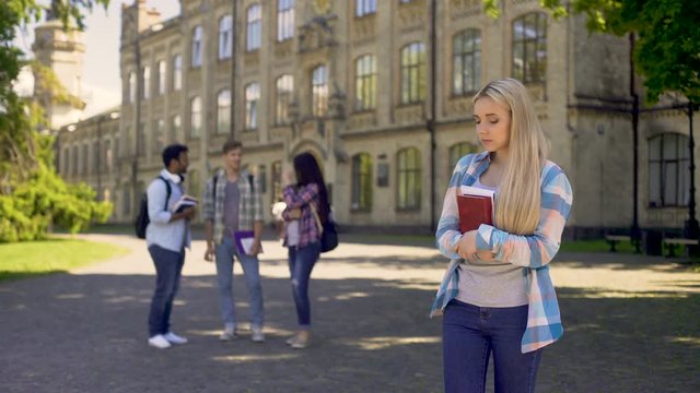 Lonely girl standing away from friends, upset about gossips at university