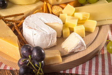 Assorted cheeses on round wooden board plate. Camembert cheese, cheese grated bark of oak, hard cheese slices, walnuts, grapes, crackers, bread, figs