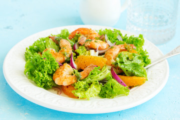 A plate of lettuce, with slices of orange, red onions, and prawns with vinaigrette dressing. A dietary dish.