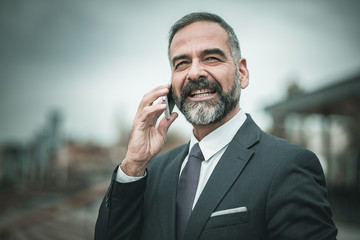 Smart senior business man, an elderly entrepreneur and business owner, talking over his cell phone in an outdoors urban area