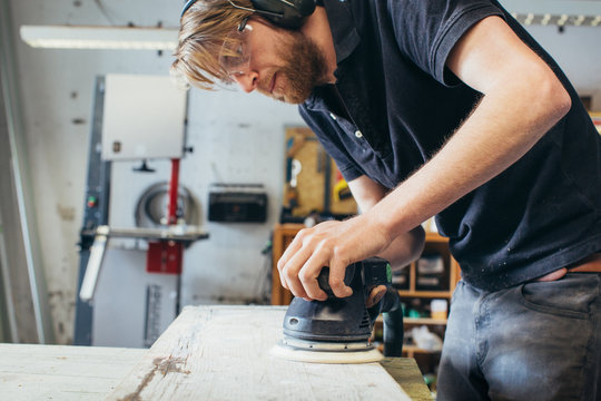 Carpentry - Young Carpenter Wearing Safety Glasses Sanding Wood Plank With Random Orbital Sander