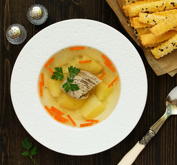 Meat and vegetable soup with parsley in a bowl on a dark background. View from above.