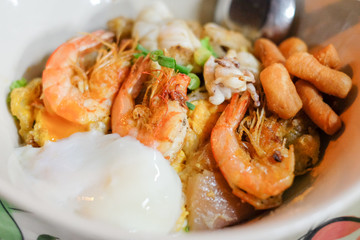 Fried rice noodle with chicken, soft-boiled egg and seafood serve on white bowl.