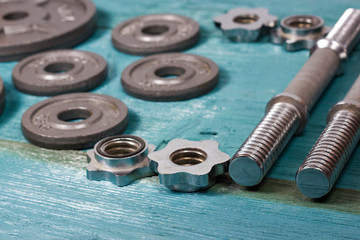 Close up of metallic weight plates on wooden floor and dumbbells in background