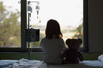 Silhouette of child patient and teddy bear looking through the hospital window