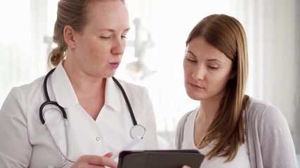 Female professional doctor at work. Woman physician with stethoscope consulting patient in modern clinic. Showing something on tablet