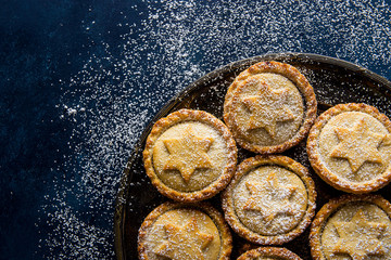 Traditional British Christmas Pastry Dessert Home Baked Mince Pies with Apple Raisins Nuts Filling Golden Shortcrust Powdered on Vintage Metal Plate Dark Blue Snowy Background Top View Copy Space © olindana